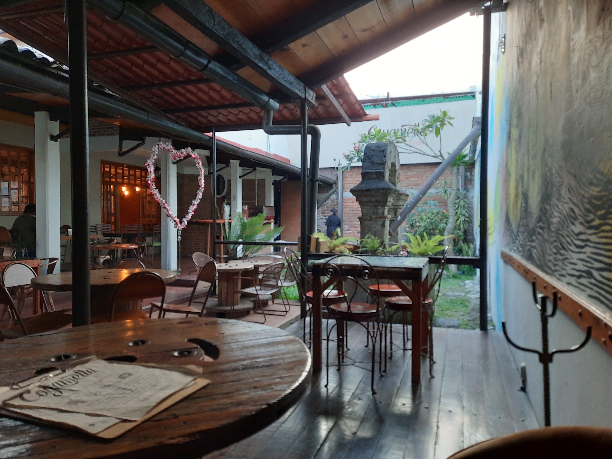 Covered café patio with wooden tables, chairs, and a menu on a foreground table.
