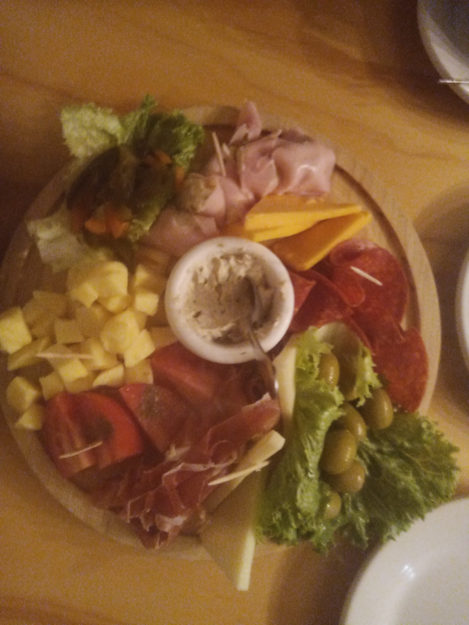 A shared platter of sliced meats, cheeses, olives, greens, and dip.